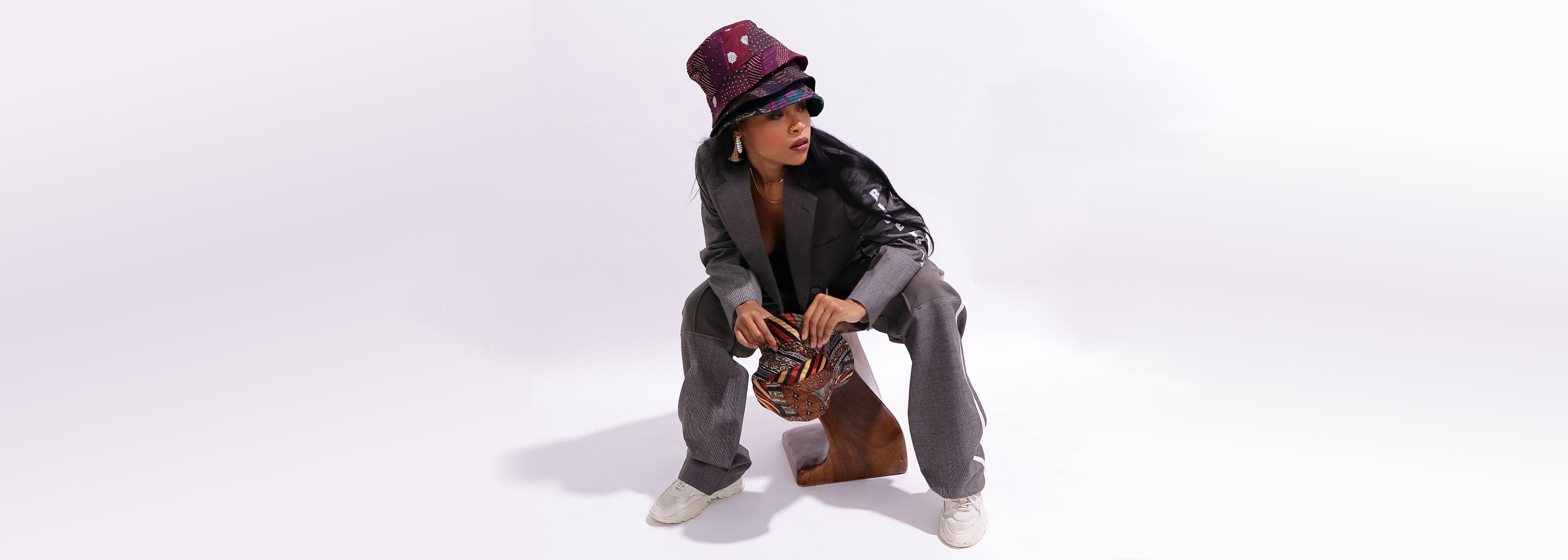 black women wearing suit sitting on wooden stool wearing multiple bucket hats made from ties